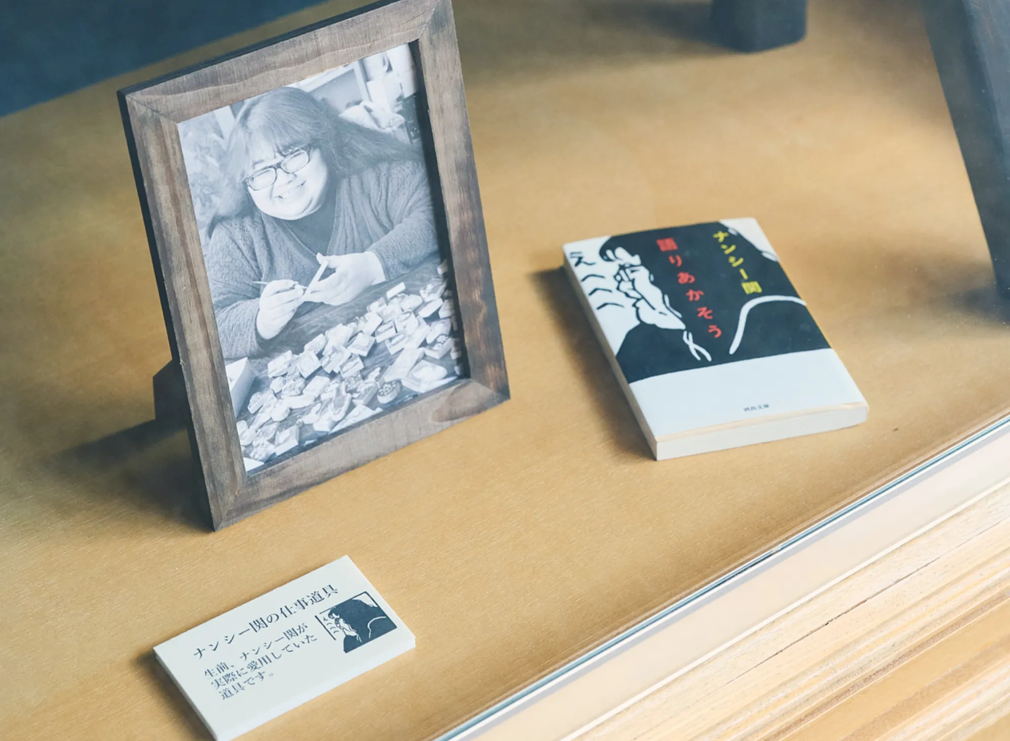 浅虫温泉 椿館の「ナンシー関 展示」。制作中の笑顔を捉えた肖像写真と、コラムニストとしての足跡を刻む著書。展示された仕事道具とともに、彼女の温かな面影と類まれなる才能を今に伝えるコーナー