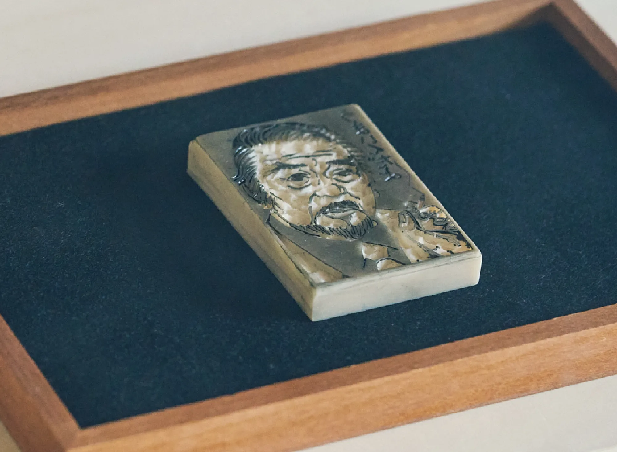 浅虫温泉 椿館の「ナンシー関 展示」カルーセル6枚目。黒いマットに静かに置かれた消しゴム版画の原版。著名人の特徴を鮮烈に描き出した精緻な彫り跡から、カッター一本で時代を射抜いた彼女の圧倒的な手仕事の凄みが伝わる