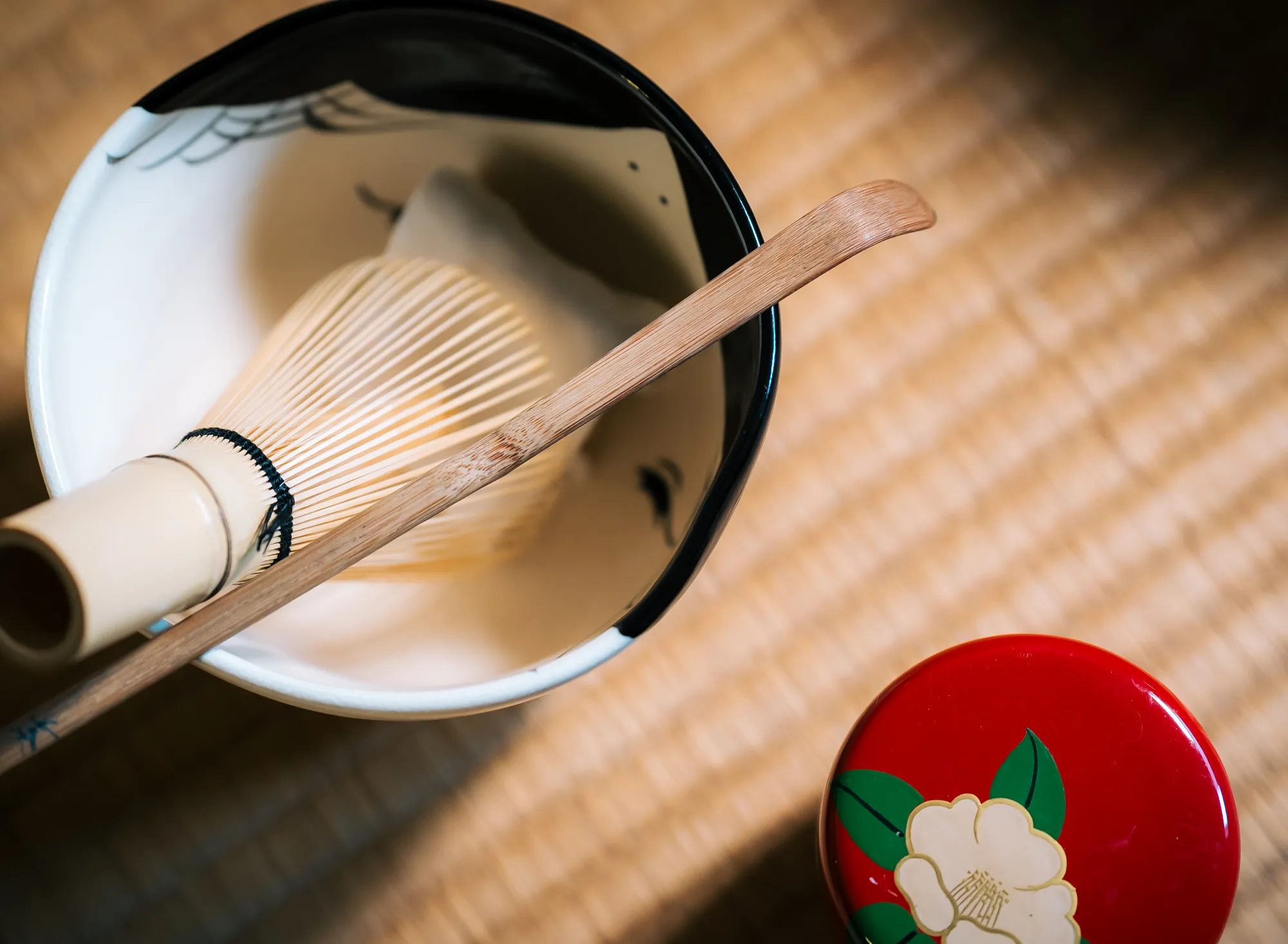 浅虫温泉 椿館の茶道体験。宿の象徴である椿をあしらった赤い棗（なつめ）と、職人技が光る茶筅・茶杓。畳の上で静かに出番を待つ、凛とした美しさの茶道具たち