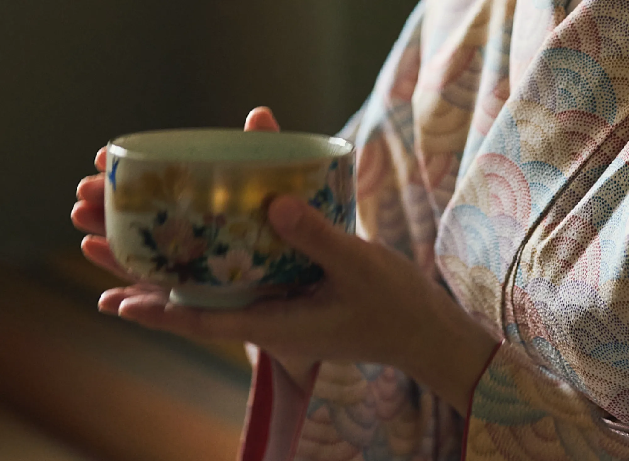 浅虫温泉 椿館の茶道体験。金彩と花々が描かれた美しい茶碗を、両手で大切に包み込む手元のアップ。青海波模様の柔らかな着物と道具が織りなす、和の感性をひらく穏やかなひととき