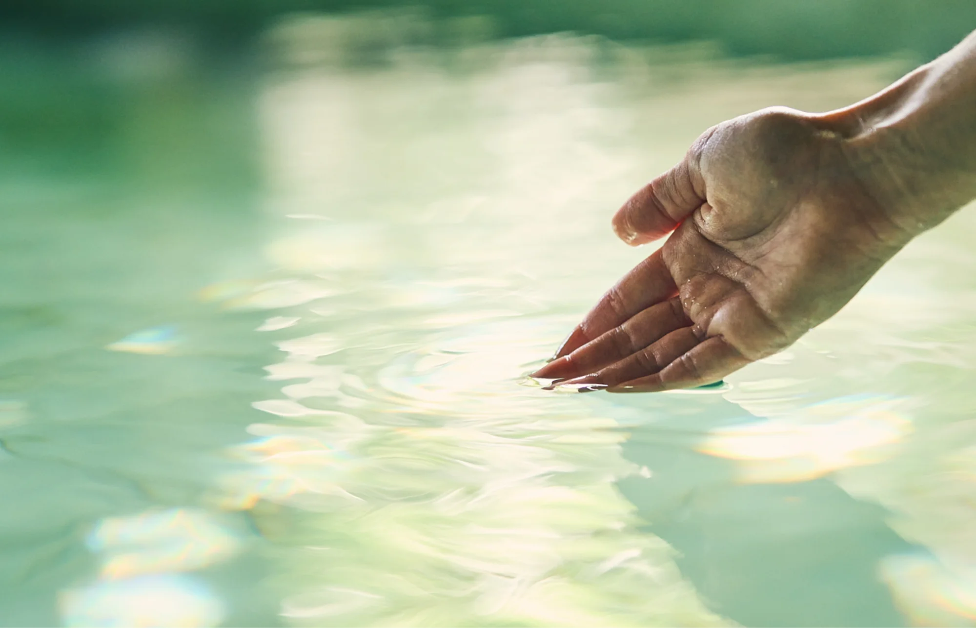 浅虫温泉 椿館の源泉かけ流しの湯にそっと手を触れる様子。澄み切った湯面に広がる柔らかな波紋と、古くから名湯として愛されてきた温泉の温もりが伝わる一枚。400余年の歴史の中で旅人の疲れを癒やしてきた、肌に優しい泉質と至福のひとときを象徴するビジュアル