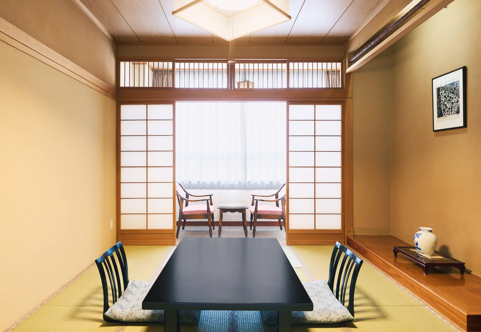 浅虫温泉 椿館の「和室」。畳の肌触りが心地よい開放感あふれる空間で、布団で眠る懐かしさと安らぎを体感できる。広縁の椅子に座り、棟方志功の作品が飾られた落ち着いた雰囲気の中で過ごす旅のひととき