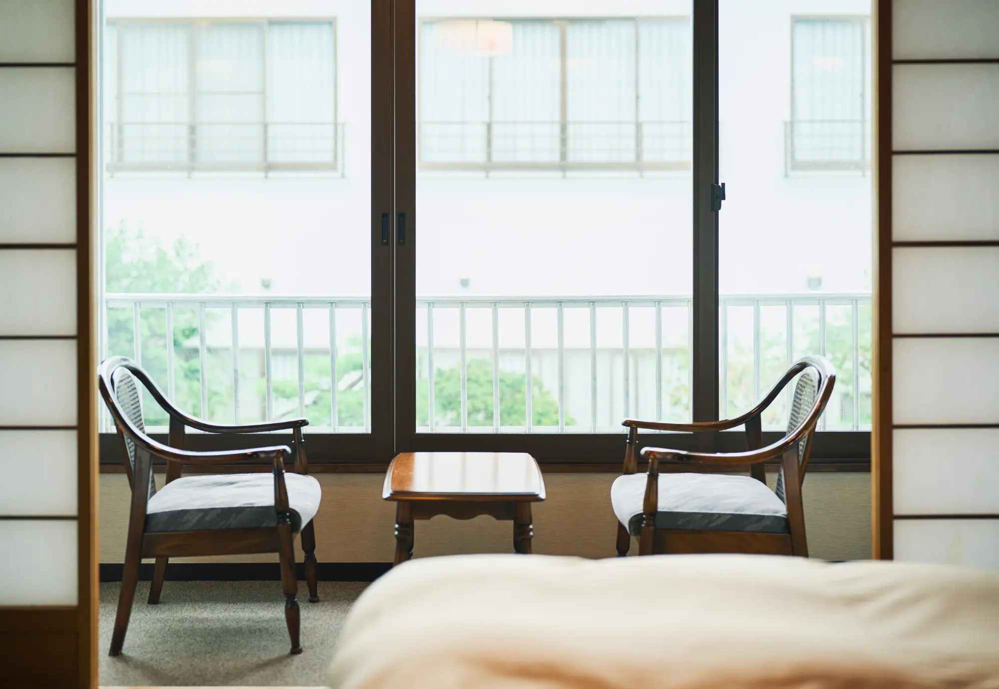 浅虫温泉 椿館の「和室10畳ベッド（2F）」にある広縁のくつろぎスペース。窓辺に配されたクラシックな椅子に腰掛け、外の景色を眺めながら静かな旅の時間を愉しめる
